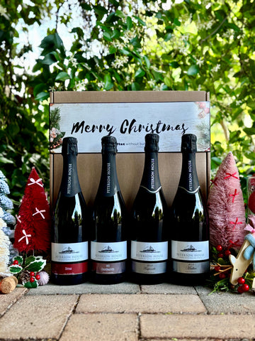 Four bottles of wine in a decorative box with 'Merry Christmas' text, surrounded by festive decorations. Huntervalley sparkling wine Peterson House 